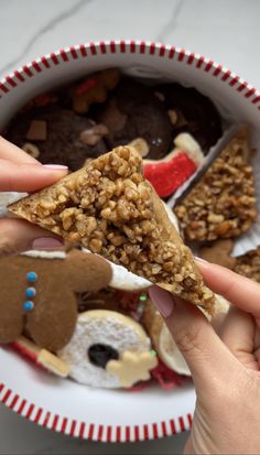 a person holding up a piece of food in front of a plate with cookies and candies on it