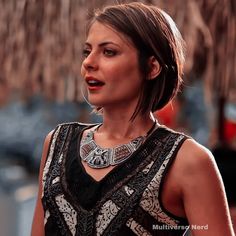 a woman wearing a black and white dress standing in front of a building with a necklace on it's neck