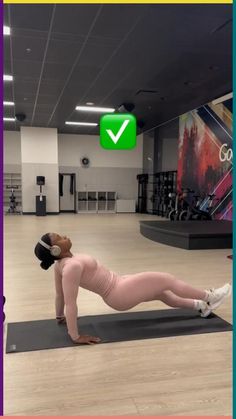 a woman is doing push ups on a yoga mat in an empty gym with a green check mark above her head