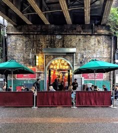 people are sitting at tables under green umbrellas