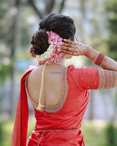 a woman wearing a red sari with flowers in her hair and holding her hands to her head