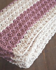 a pink and white crocheted blanket laying on top of a wooden floor next to a brown table