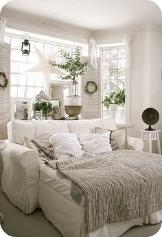 a living room filled with white furniture and lots of plants in the window sill