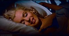 a woman laying in bed with her eyes closed and mouth wide open, smiling at the camera