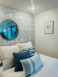 a white bed topped with pillows next to a round mirror on the wall above it