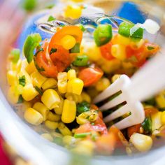 a fork in a glass bowl filled with corn and vegetables