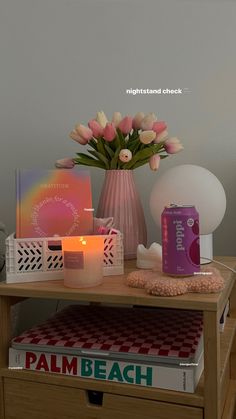 a wooden table topped with books and a vase filled with pink flowers next to a candle