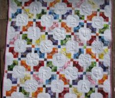 a colorful quilt is hanging on a wooden wall in front of a brick wall and floor