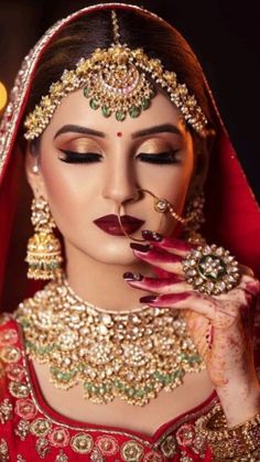 a woman in a red and gold bridal outfit with her hands on her face