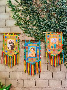 three colorful wall hangings on a brick wall next to a green plant and potted plant