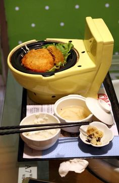 a yellow toilet bowl filled with food on top of a table next to chopsticks