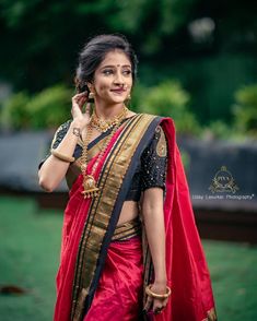 a woman in a red and gold sari is talking on her cell phone while standing outside