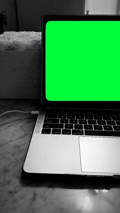 an open laptop computer sitting on top of a marble table with a green screen in front of it