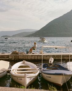 two small boats tied up to the dock with a man sitting on top of one