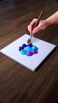 a person using a brush to paint on a piece of paper with blue and purple shapes