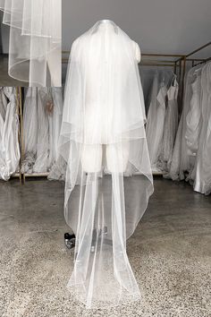 a mannequin wearing a white veil in front of several dresses on hangers