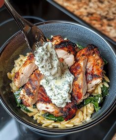 a bowl filled with chicken and pasta on top of a counter next to a knife