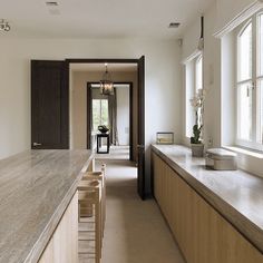 an empty kitchen with wooden cabinets and marble counter tops in front of two large windows