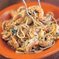 someone is eating pasta with shrimp and lemons in a orange bowl on the table