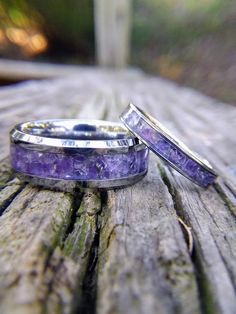 two wedding bands with amethyst purple stone inlays sitting on a wooden surface