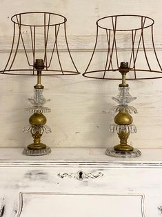 two metal lamps sitting on top of a white dresser