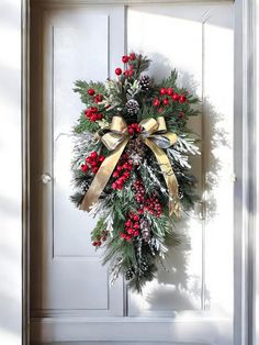 a wreath hanging on the front door of a house with red berries and pine cones