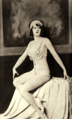 an old photo of a woman in a bathing suit sitting on a bed with her legs crossed