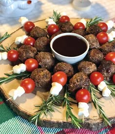 a platter filled with meatballs and tomatoes on top of a wooden board next to a dipping sauce