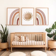 a baby crib with two pictures on the wall above it and some potted plants