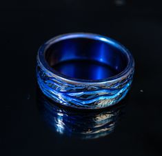 a blue ring sitting on top of a black surface with water in the middle and waves coming out of it