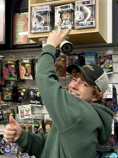 a man in a green hoodie is pointing at some items on the wall behind him