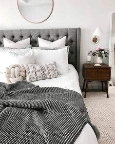 a white and black bedroom with a round mirror above the bed