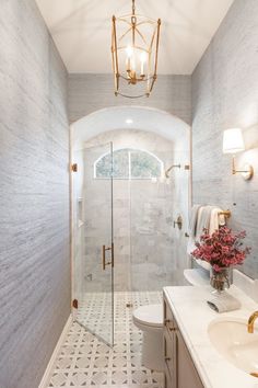 a bathroom with a walk in shower next to a white toilet and sink under a chandelier