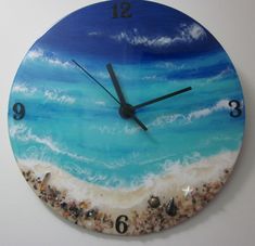 a clock that is on the wall with sand and sea shells in front of it