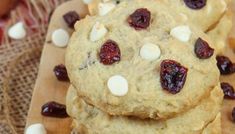 cookies with cranberries and white chocolate chips are stacked on a cutting board, ready to be eaten