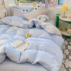 a bed with blue sheets, pillows and stuffed animals on top of it in front of a window