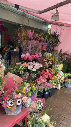 a bunch of flowers that are sitting on a table in front of a building with a pink awning