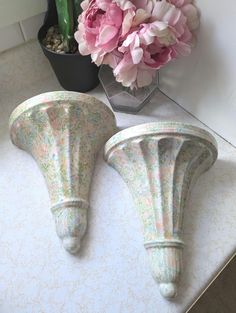 two vases with pink flowers in them on a white counter top next to a potted plant