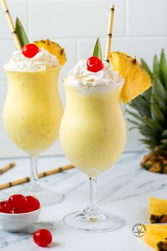 two cocktails with pineapple and whipped cream garnished with cherries on the rim