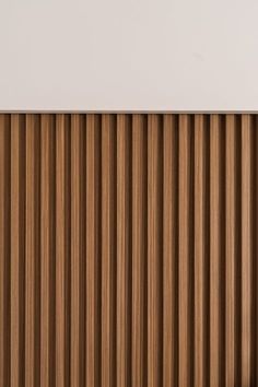 a close up view of a wooden slatted wall with white walls in the background