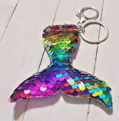 a mermaid tail shaped keychain on a white wood floor with a metal hook