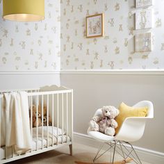 a teddy bear sitting in a rocking chair next to a baby crib and wallpaper