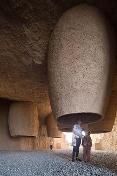 two people are standing under a large object in the middle of a room filled with rocks