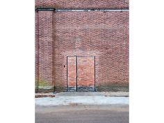 an open gate in front of a brick wall on the side of a building with no doors