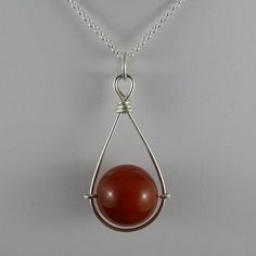 a pendant with a red stone hanging from it's side on a silver chain