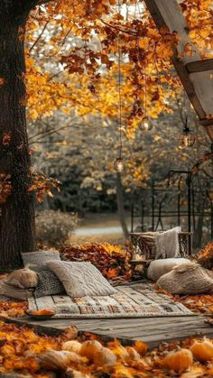 a bed sitting under a tree filled with lots of fall leaves on top of it