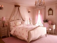 a bedroom with pink walls and curtains on the windowsills, a chandelier above the bed