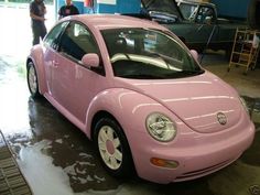 a pink car parked in a garage next to other cars and people standing around it