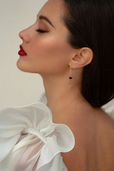 a woman with red lipstick and large earrings on her neck, wearing a white blouse