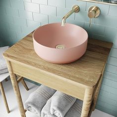 a pink bowl sink sitting on top of a wooden table next to towels and a towel rack